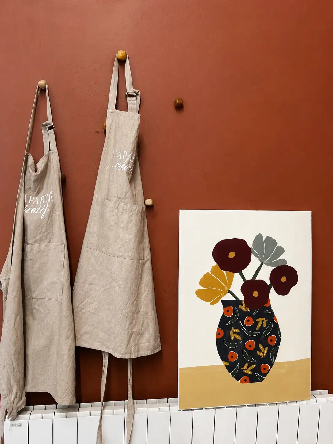 Tabliers de L'Aparté Créatif suspendus sur le mur terracotta de l'atelier